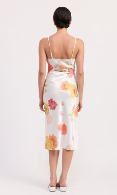 A person faces away, wearing the V-Neck Floral Print Midi Slip Dress with a sheath silhouette and white shoes, standing against a plain background.