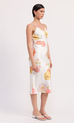 A woman wears the V-Neck Floral Print Midi Slip Dress with thin straps and white heeled sandals, showcasing a graceful sheath silhouette against a plain background.