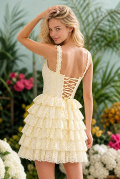 A woman stands outdoors in the Eyelet Yellow Short Casual Dress: Isla, surrounded by green plants and colorful flowers.