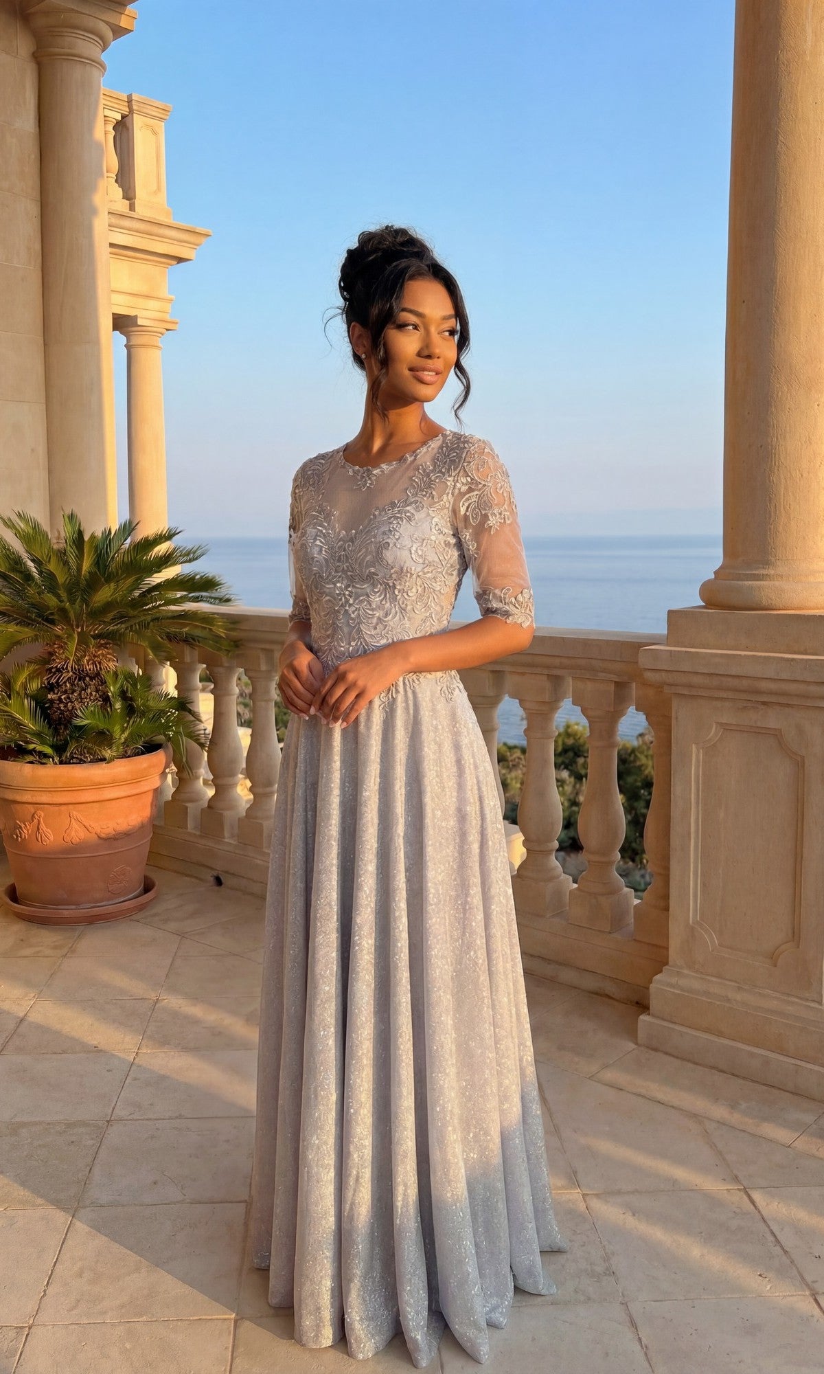 A woman in the silver Long Formal Dress: Chicas J006 stands on a balcony with stone columns, gazing at the sea during sunset.