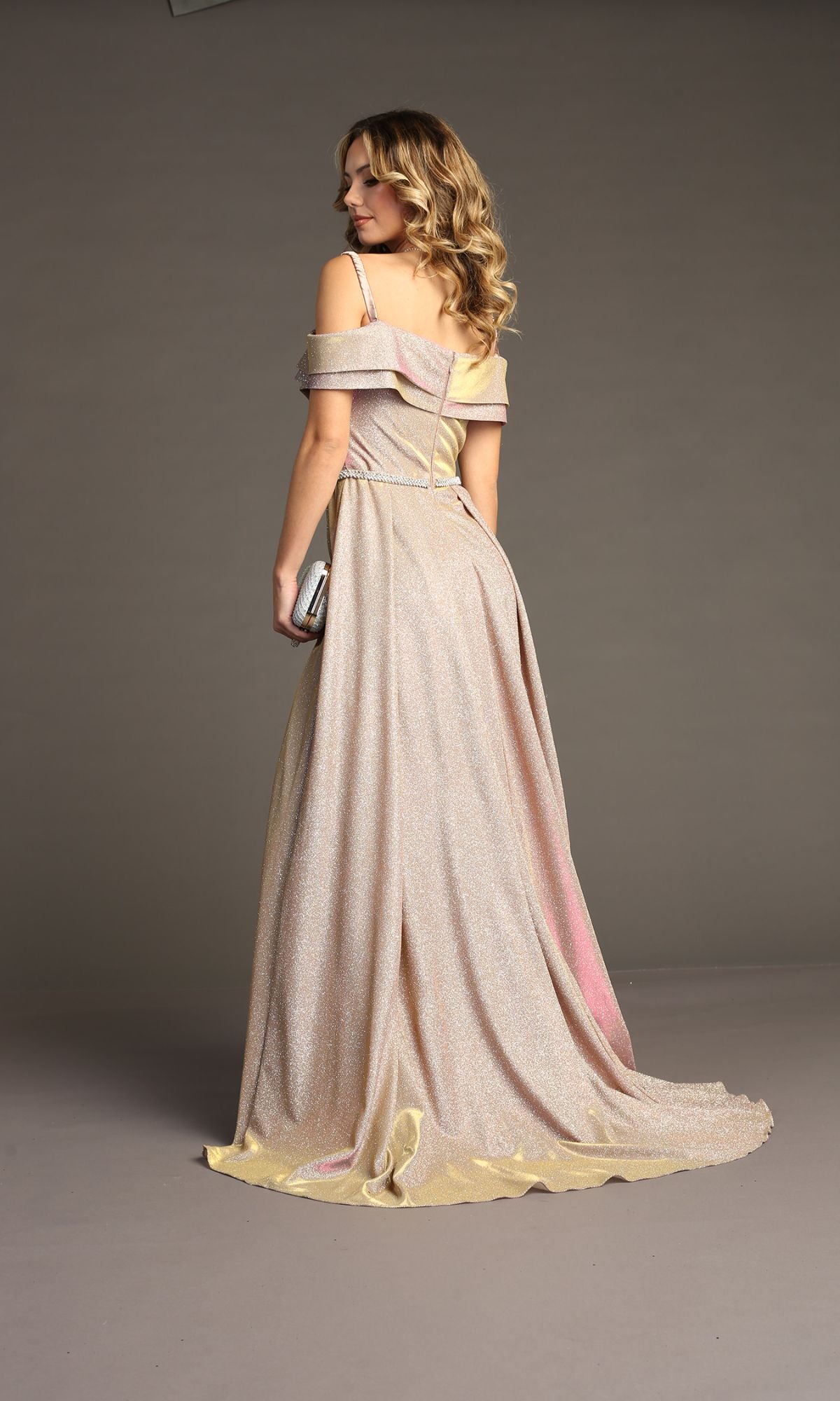 A woman wearing the Off-Shoulder Long Glitter Prom Dress: Chicas J008 stands facing away, holding a silver clutch against a plain background.