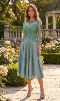 A woman wearing the Chicas J040 midi wedding guest dress in sage, featuring elegant lace details and sheer sleeves, stands on a garden path surrounded by flowers and greenery.