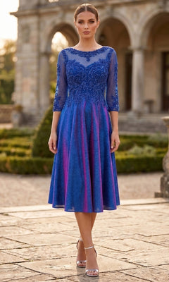 A woman wearing the Chicas J040 Midi Wedding Guest Dress in royal blue, featuring sheer sleeves and floral embroidery, stands outdoors on a stone pathway in front of a formal building.