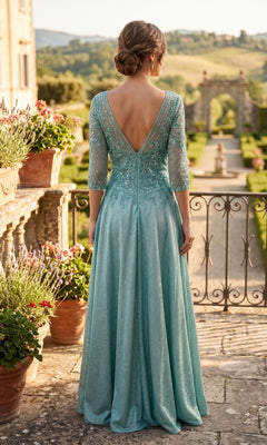 A woman stands on a terrace overlooking a garden, her back to the camera, wearing the Chicas J052 long formal dress in light blue with sheer sleeves.