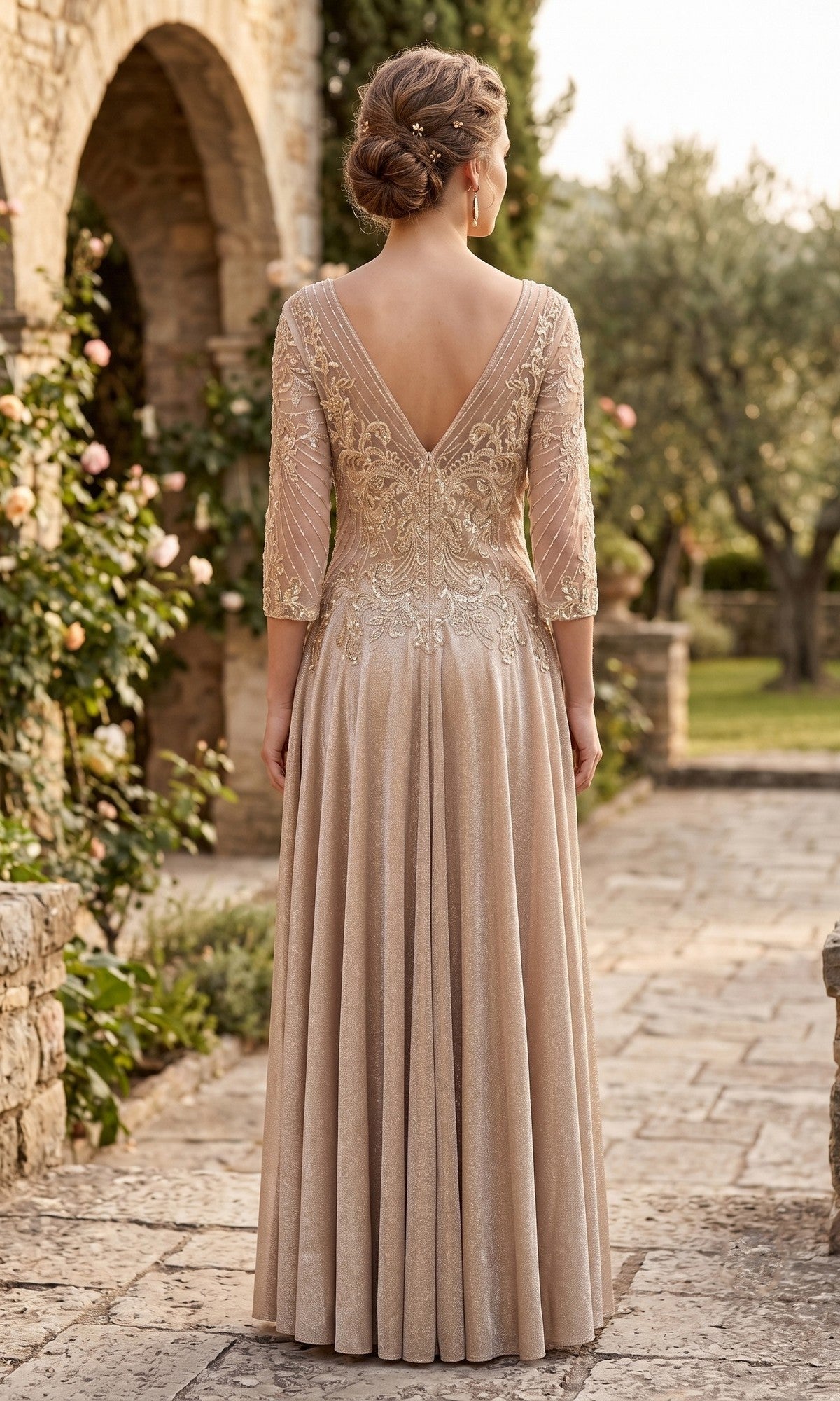 Wearing the Long Formal Dress: Chicas J052 in an elegant, floor-length champagne hue with lace details, a woman stands outdoors on a stone path, facing away.