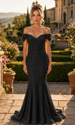 A woman stands outdoors in a formal garden setting, wearing the Chicas J066 long prom dress in black—an off-the-shoulder design featuring a fitted mermaid silhouette with glittering details and a dramatic flared hem.