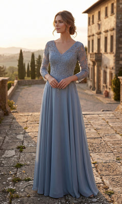 A woman in a slate blue Chicas J070 Long Prom Dress stands on a stone path outdoors near a large building at sunset, her elegant, long-sleeved chiffon evening gown perfect for formal occasions.