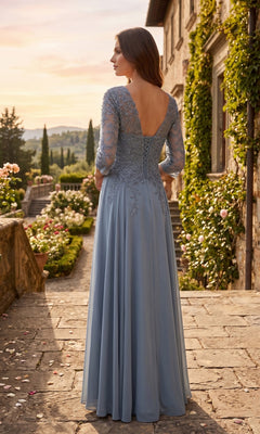 A woman wearing the Long Prom Dress: Chicas J070, a light blue chiffon evening gown with lace sleeves, stands outdoors on a stone path beside a greenery-clad building, facing away from the camera.