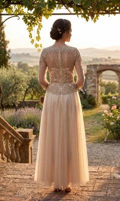 A graceful woman, dressed as the mother of the bride in the Chicas J082 Long Prom Dress featuring elegant long sleeves and an embellished lace bodice, stands on a stone terrace, facing away as she overlooks a scenic garden at sunset.