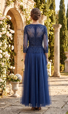 A woman in the elegant Chicas J082 Long Prom Dress, featuring a beautifully embellished bodice, stands outdoors on a stone path amid blooming flowers and lush greenery with stone columns in the background—an ideal choice for the mother of the bride.