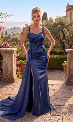 A woman wearing the Chicas J092 Long Prom Dress in navy, featuring delicate lace straps and a thigh-high slit, stands on a stone terrace in a garden setting.