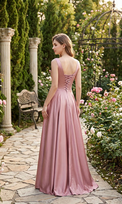 A woman wearing the Chicas J112 long prom dress in pink satin stands on a stone path in a garden surrounded by roses, columns, and lush greenery.