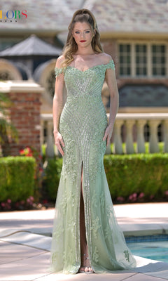 A woman stands outdoors in front of a pool and landscaped garden, wearing the Colors Dress J131—an off-shoulder beaded prom dress with a front slit in light green.