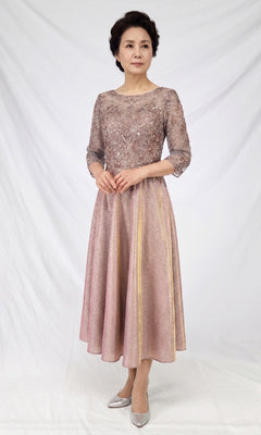 A woman wearing the Chicas J152 Modest Midi Wedding Guest Dress in rose gold, featuring embroidery and sheer sleeves, stands against a white backdrop paired with silver heels.