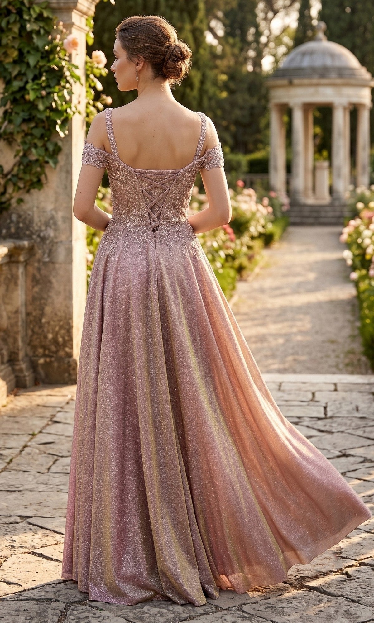 A woman wearing the Long Prom Dress: Chicas J169—a shimmery pink off-the-shoulder gown with a glitter A-line skirt—stands on a stone path in a garden, facing away from the camera, with a gazebo visible in the background.