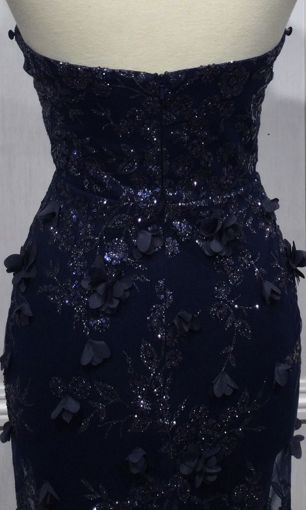 Close-up of the back of the Strapless Long Pageant Dress with Cape J834 in dark blue, shown on a mannequin. Features a sweetheart neckline, floral appliqué, and glittery details.