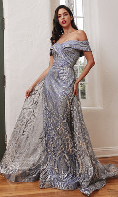 A woman stands indoors wearing the Long Prom Dress with Glitter-Print Overskirt J836, an off-shoulder silver and lilac evening gown with baroque glitter prints and a long, sheer, flowing train.