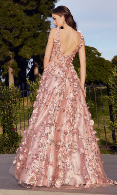 A woman stands outdoors in the Long Glitter-Floral A-Line Prom Ball Gown J838, a floor-length pink dress with floral glitter appliqué, deep V-back, and flared skirt. Trees and greenery fill the background.