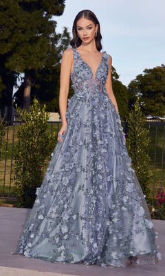 A woman stands outdoors among green trees and shrubs in the Long Glitter-Floral A-Line Prom Ball Gown J838, a sleeveless light blue dress featuring floral appliqués and a deep V neckline.