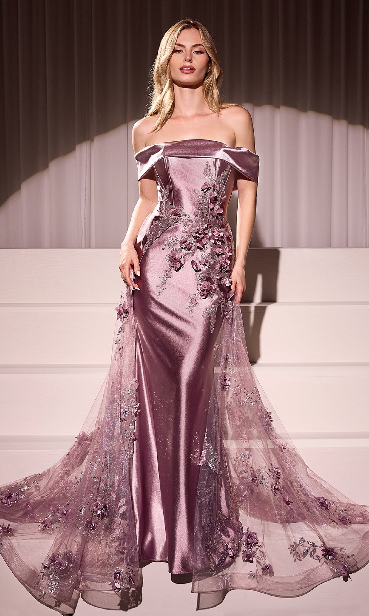 A woman wears the Ladivine J876, a mauve satin long prom dress with tulle overskirt and floral embroidery, standing before white steps and draped curtains.