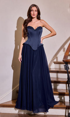 A woman stands indoors beside a stairway, wearing the Ladivine J891 long prom dress in navy. This strapless gown features a corset bodice and flowing chiffon A-line skirt.