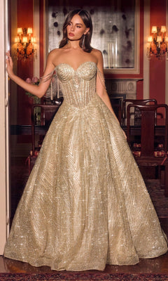 A woman stands indoors in an elegant, dimly lit room with chandeliers and classic decor, wearing the Ladivine J915 long prom dress in gold—a strapless ball gown featuring glitter tulle, crystal beadwork, and chain details on the arms.
