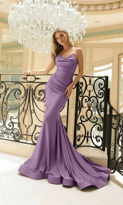 A woman wearing the Jessica Angel 2424 Strapless Mermaid Formal Dress poses indoors near an ornate railing and a large crystal chandelier.