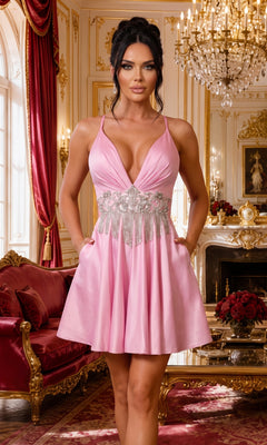A woman wearing the Jessica Angel JA2331 short homecoming dress in Bubblegum, featuring a sleeveless, V-neck fit-and-flare silhouette with a beaded waistband, stands in an ornate gold-trimmed room adorned with a chandelier, red sofa, and flowers.
