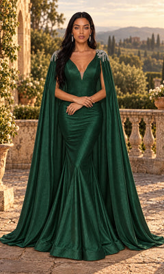 A woman stands outdoors on a stone terrace with lush greenery in the background, wearing the Jessica Angel JA896 long prom dress in Hunter—a fitted mermaid gown with a matching cape.