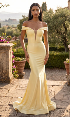 A woman stands outdoors on a stone pathway lined with greenery and potted flowers, wearing the Jessica Angel JA933 long prom dress in pale yellow—a fitted gown with an off-the-shoulder neckline, deep V, and elegant trumpet silhouette.