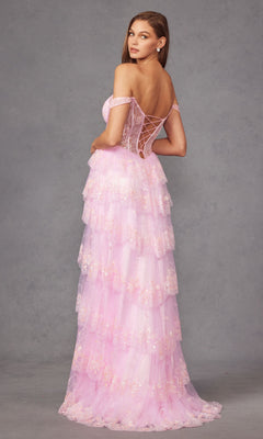 A woman models the Long Prom Dress JT2453K by Juliet, a pastel pink, off-the-shoulder gown with a lace-up back, sequin accents, and tiered ruffle tulle, posed against a plain grey background.
