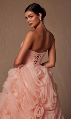 Woman wearing the Strapless Peach Prom Ball Gown Nox Anabel JQ1037 with ruffled details and lace-up back, posing with her head turned over her shoulder against a neutral background.