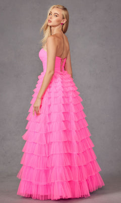 A woman poses against a plain gray background in the Long Prom Dress JT2456H by Juliet, a strapless bright pink ruffle tulle ball gown with an empire waist, her head turned to the side.