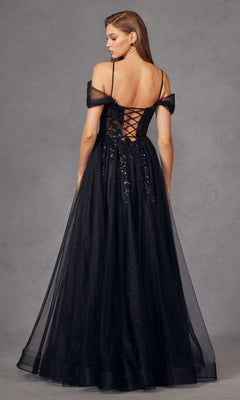 A woman stands against a gray background in the Sheer-Waist Long Prom Ball Gown: Juliet JT2466A, a black off-the-shoulder A-line dress with a lace-up back and sheer overlay—perfect for timeless elegance at any special event.