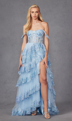 A woman models the Juliet JT2467K off-the-shoulder ruffled prom dress in light blue, featuring sparkling embellishments and a high slit, standing against a gray studio backdrop.