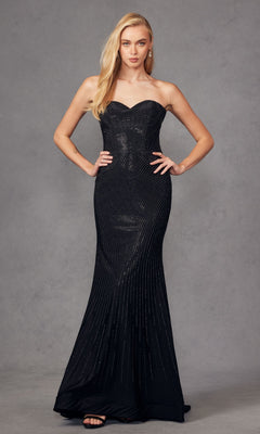 A woman stands against a gray background wearing the Strapless Long Sequin Prom Dress: Juliet JT2472R, featuring shimmering sequins, paired with black high-heeled sandals.