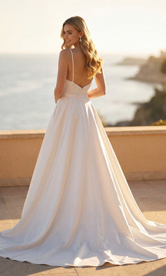 A woman wearing the Long Formal Dress: Juliet JT2603CW stands outdoors, facing away with her head turned, overlooking a sunlit coastal landscape.