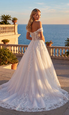 Wearing the Juliet JT2634LW long formal dress, a woman stands on a terrace overlooking the ocean at sunset, surrounded by potted plants.