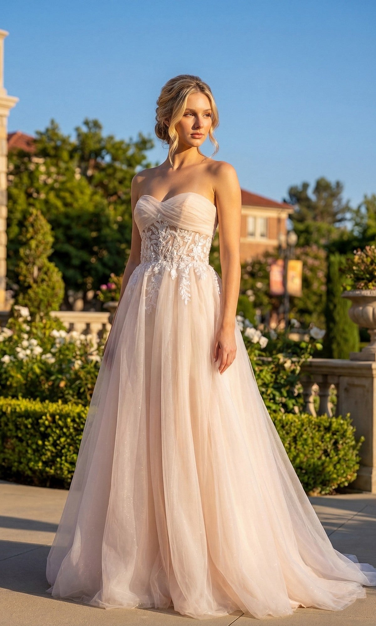 A woman stands outdoors in sunlight wearing the Juliet JT2702AW Long Prom Dress in nude, featuring a strapless, flowing A-line tulle skirt and a sheer floral lace corset bodice.