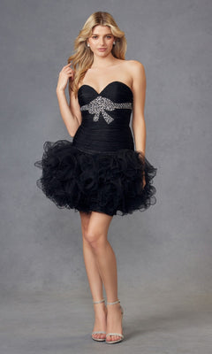 A woman poses against a gray background in the Short Black Hoco Dress: Juliet JT705, featuring a strapless sweetheart neckline, ruffled tulle skirt, and a jeweled bow at the waist.