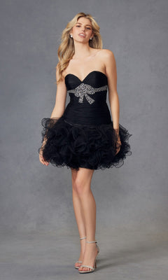 A woman stands against a gray background wearing the Juliet JT705 short black hoco dress, which is strapless with a ruffled tulle skirt and a rhinestone bow.