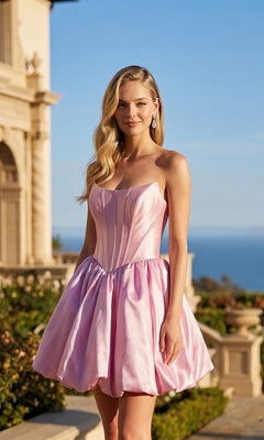 Wearing the Juliet JT7184U short homecoming dress in candy pink, a woman stands outdoors near a building, with gardens and the ocean visible in the background under a clear sky. The strapless dress features an elegant A-line skirt.