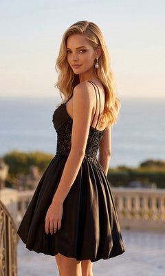 Wearing the Juliet JT7186A Short Homecoming Dress, a woman stands outdoors with the ocean and greenery behind her, glancing softly over her shoulder. The sleeveless black dress features a beaded bodice that catches the light, perfectly complementing its satin a-line skirt.