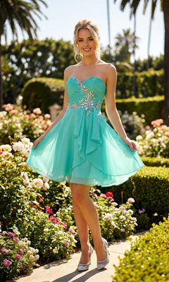 A woman stands in a garden surrounded by flowers and palm trees, smiling as she holds the skirt of the Juliet JT741 short homecoming dress—a strapless turquoise gown featuring silver embellishments and a pleated bodice.