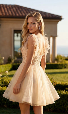 A woman wearing the Juliet JT881 short homecoming dress—a light beige, sleeveless, fit-and-flare style featuring feather details and touches of tulle—stands outdoors near a building and garden, glancing over her shoulder.