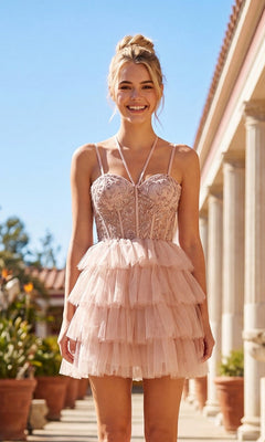 A woman smiles outdoors in front of columned architecture and potted plants, wearing the Sheer-Corset Short Ruffled Hoco Dress JT923S in buff—a strappy, tiered mini dress with lace details and an embroidered bodice.