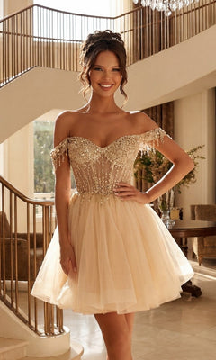A woman stands indoors wearing the Short Champagne Corset Prom Dress: Juliet JT947L, featuring an off-the-shoulder beaded bodice and tulle skirt—a stunning champagne outfit for any party.