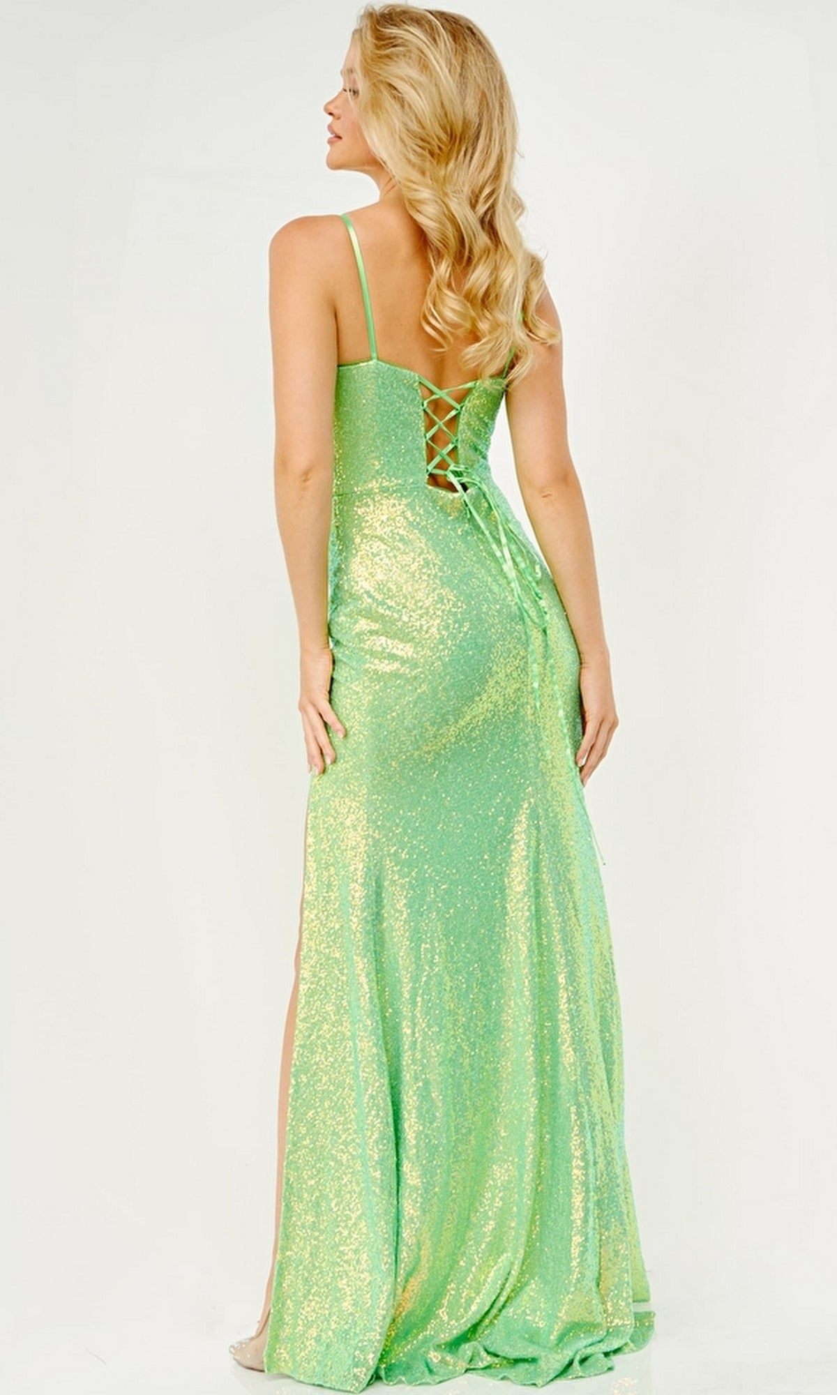 A woman with long blonde hair wears the Jovani JVN23346 long prom dress in shimmery light green, featuring a fitted silhouette, elegant lace-up back detailing, and thin straps.