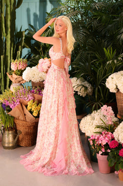 A woman with long blonde hair poses indoors among flowers and plants, wearing the Open-Back Pink Floral Maxi Dress: Juliette.