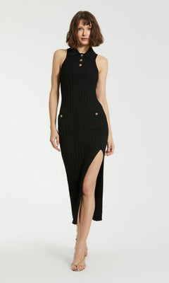 A woman wears the Mac Duggal Midi Black Knit Casual Party Dress K10030—a sleeveless, ribbed knit dress with gold buttons and a high side slit—while standing against a plain white background.